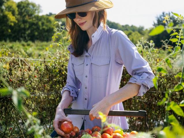 Woman in purple shirt putting vegetables in a basket.