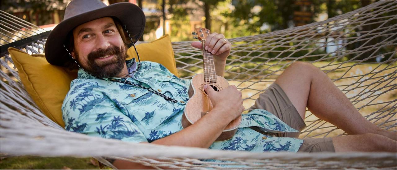 Man laying in hammock with ukulele. 