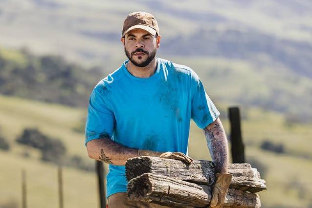 Man wearing black longtail tee carrying 2x8 wood planks over his shoulder