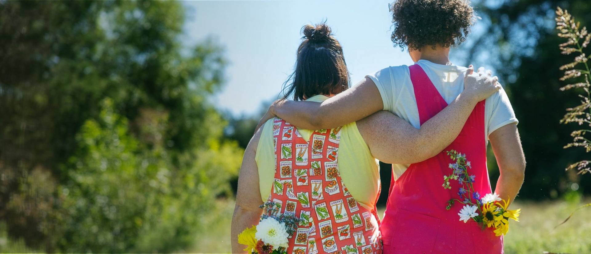 Two women wearing overalls, linking arms.