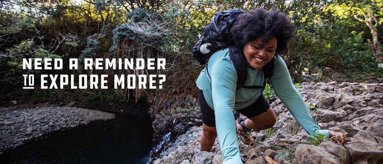 Woman in a blue shirt and black backpack climbs rocks