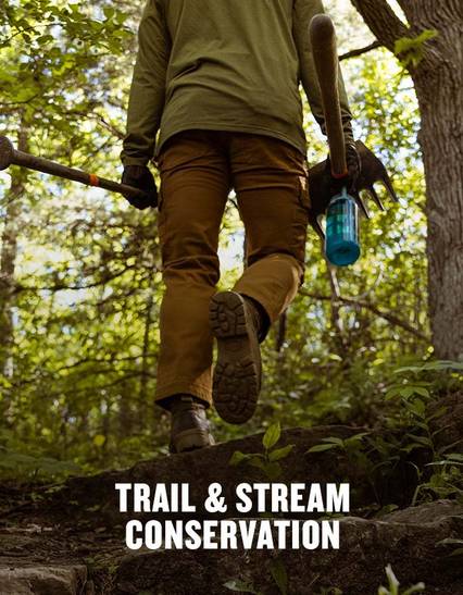 person walking in the woods with brown boots, tan pants, and a green shirt