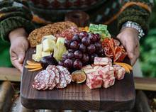 man holding a Best Made (tm) board with fruits, vegetables, cheese and meats