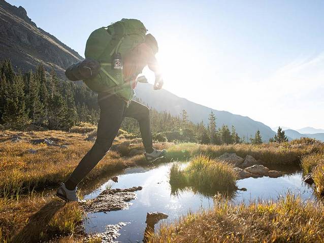 Man with hiking gear jumping over water