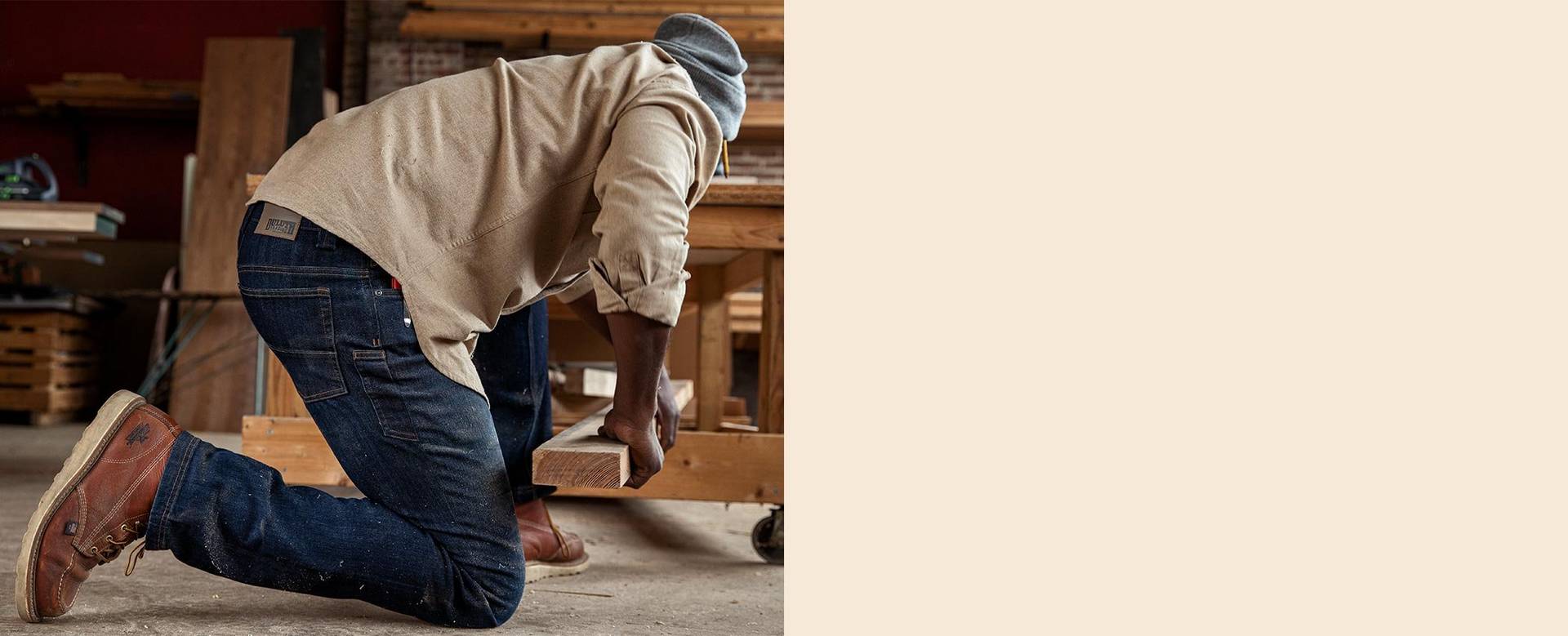 Man kneeling in denim jeans, grabbing a piece of wood