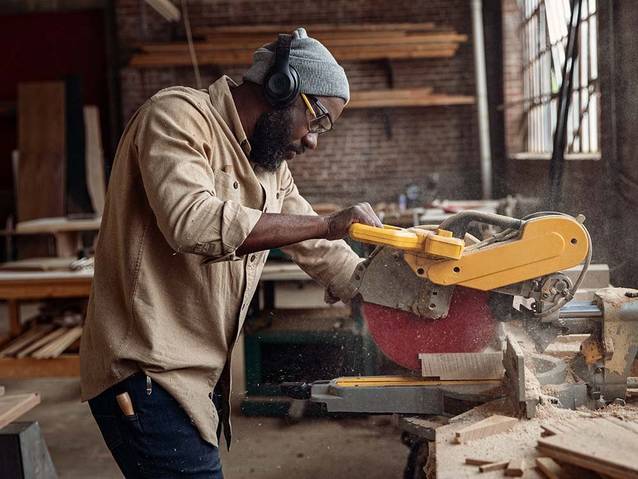 man cutting wood on a miter saw inside a workshop