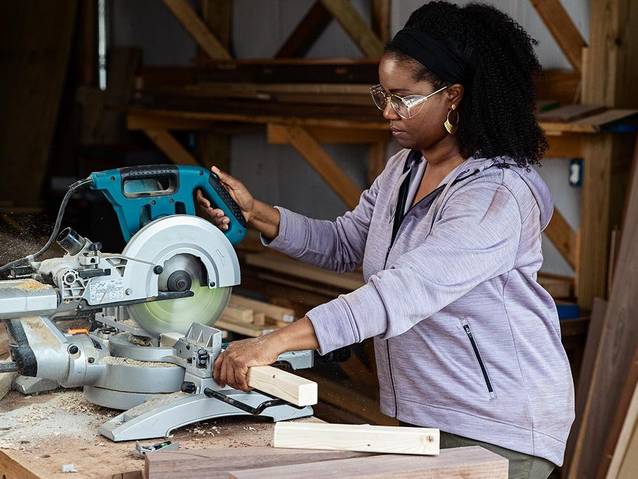 woman cutting wood on a miter saw inside a workshop