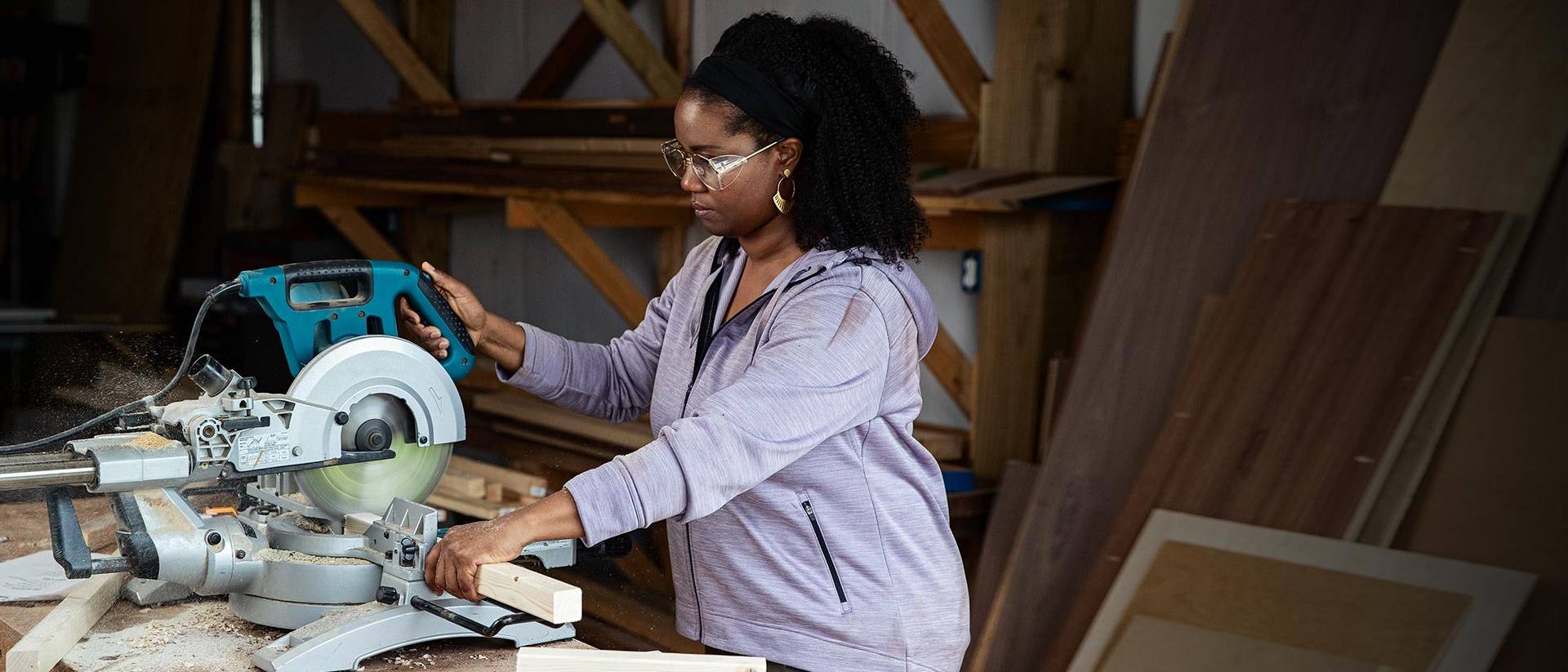 Women wearing a purple jacket, cutting a piece of wood with a saw