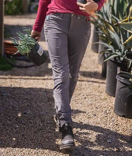 A close-up of gray pants as a woman walks holding potted plants