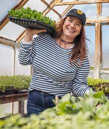 A woman in a long-sleeved striped shirt holds a flat of plants