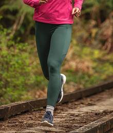 A woman in green leggings runs through a forest