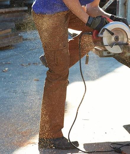 Close up of woman's brown fire hose pants while she works with a band saw