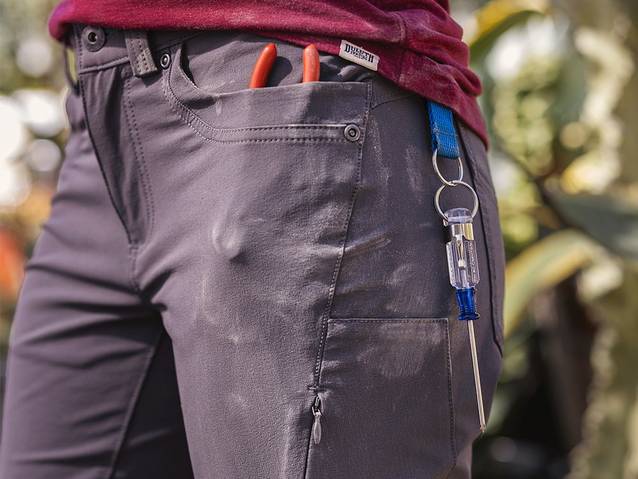 A close up on a woman wearing flexpedition pants, dirty from work with pockets full of tools.