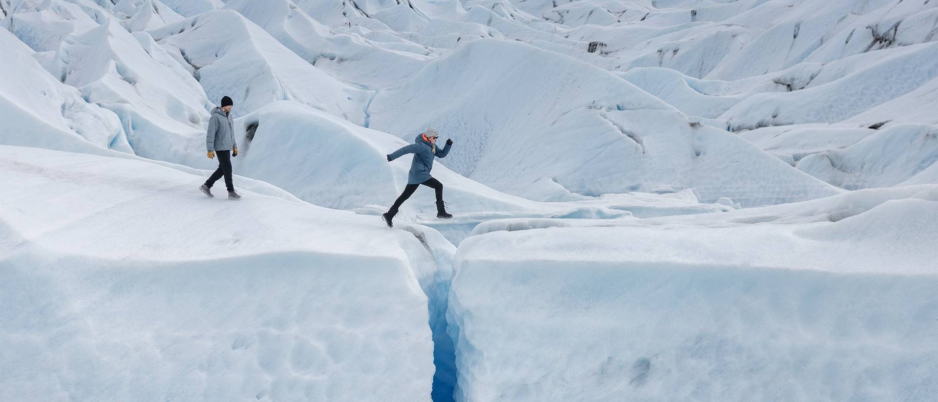 Man and woman jumping over a crevasse.