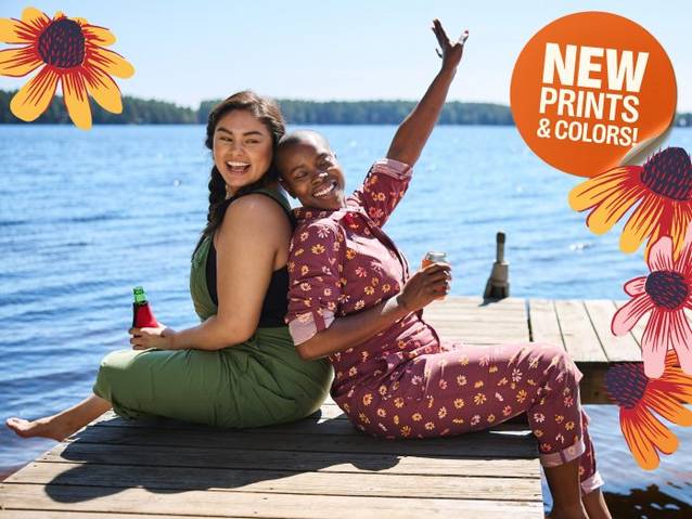 Two women wearing overalls sitting on dock.