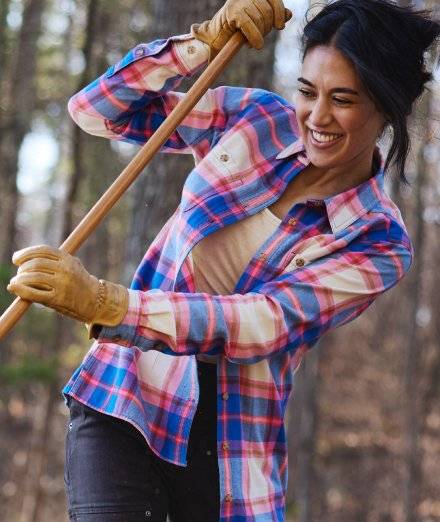 Woman wearing flannel, raking leaves outside.