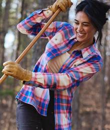 Woman wearing flannel, raking leaves outside.