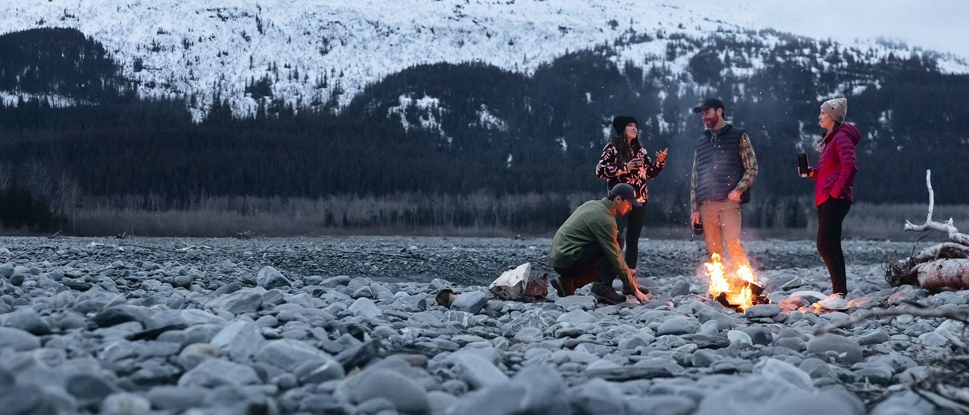 Four people standing around a campfire in the mountains.