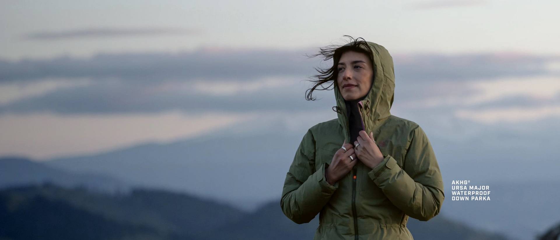 Woman standing on mountain, wearing a green hooded jacket.