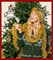Woman wearing a sweater with tinsel wrapped around her, standing in front of a Christmas tree.