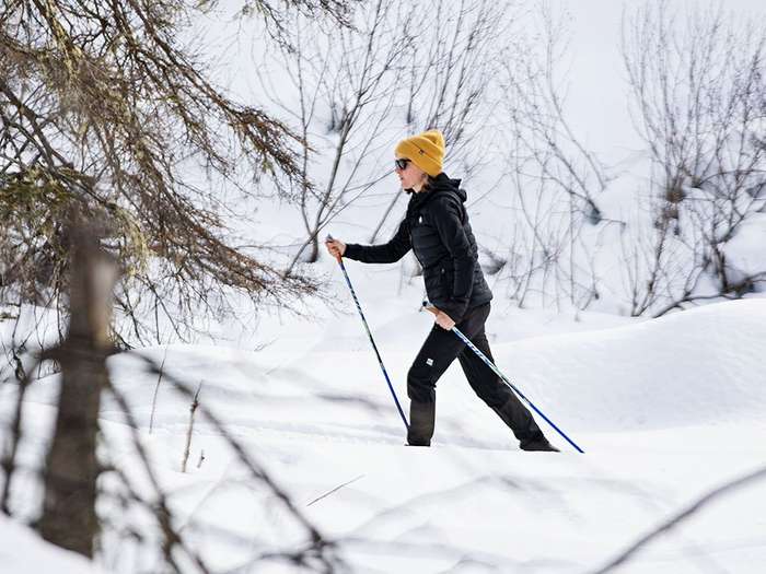 Woman cross country skiing in black pants and jacket and a yellow hat in a winter scene