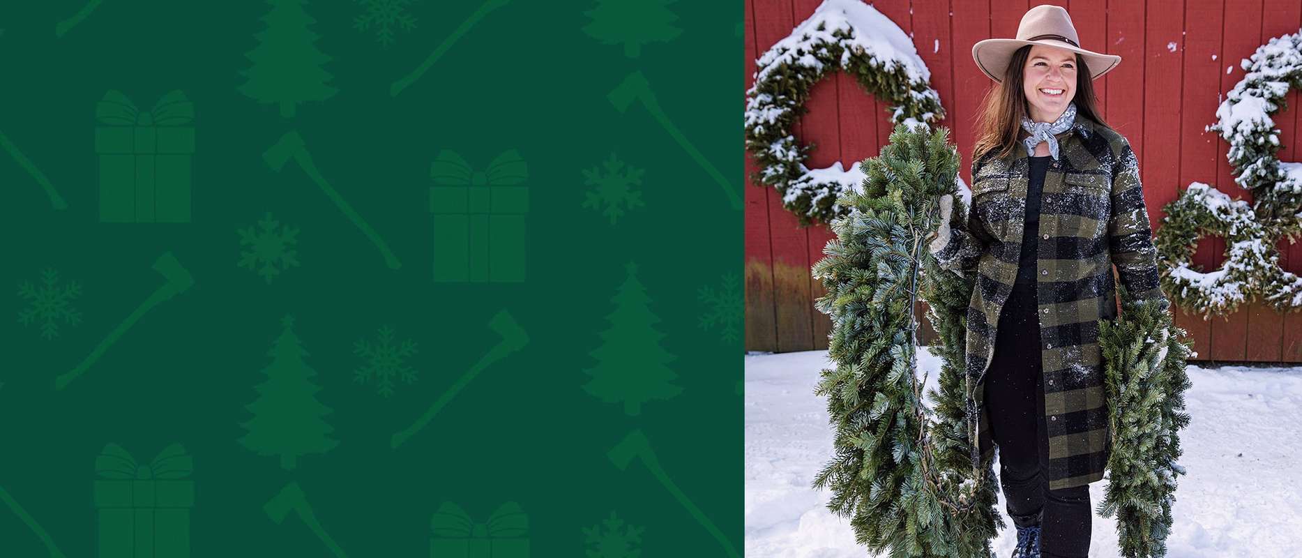 A woman in a flannel shirt holds pine wreaths in the snow in front of a red barn