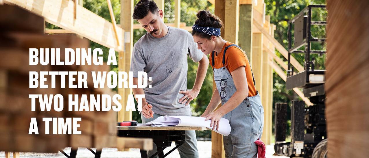 man in gray shirt standing next to woman in blue overalls looking at floor plans