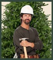 Man wearing hard hat and holding a hammer, standing in front of a Christmas tree.
