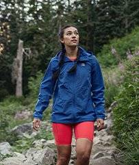 Woman wearing AKHG wind jacket, hiking on a rocky forest trail