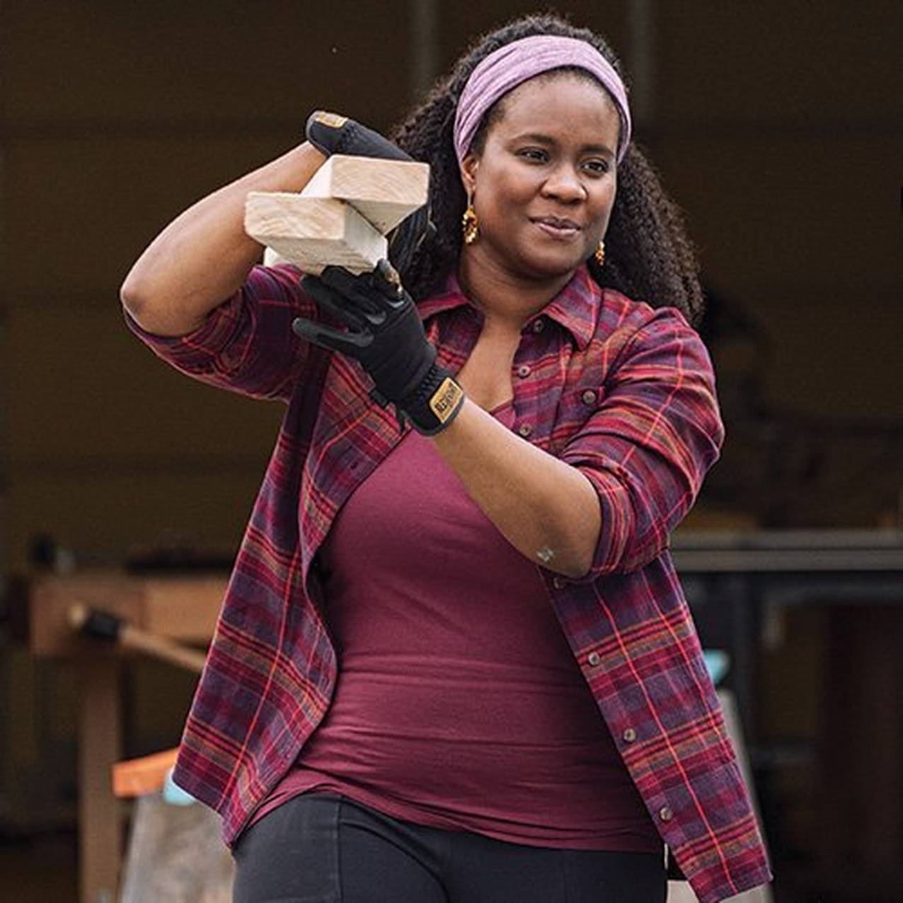 woman wearing a no yank tank under a flannel shirt, carrying lumber