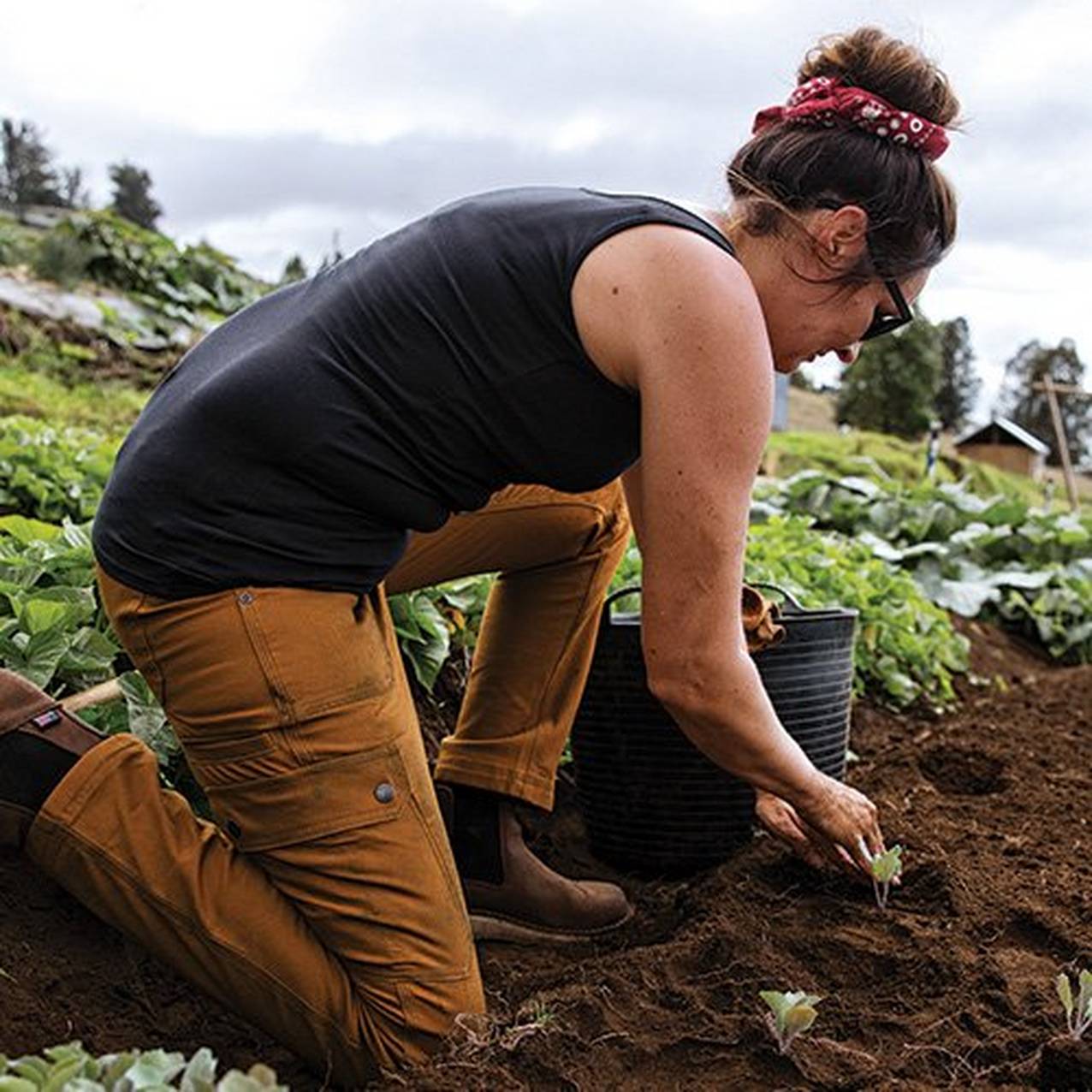 woman in a no yank tank bending over to dig in the garden