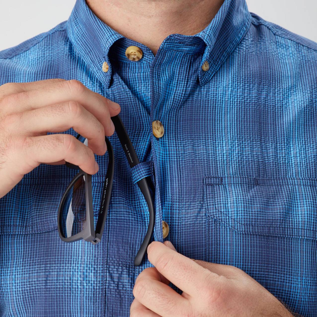 View of hands putting arm of sunglasses through loop on shirt