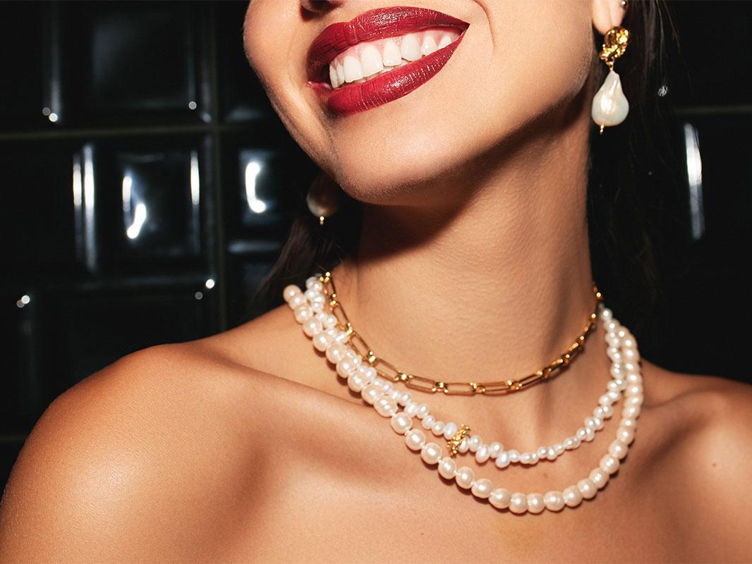 Woman in red lipstick smiling with a pearl necklace on