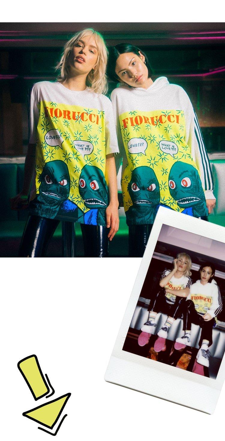 Models wearing the Adidas x Fiorucci Graphic Print Oversized T-Shirt in white and the Adidas x Fiorucci Graphic Archive Print Hoodie in white.