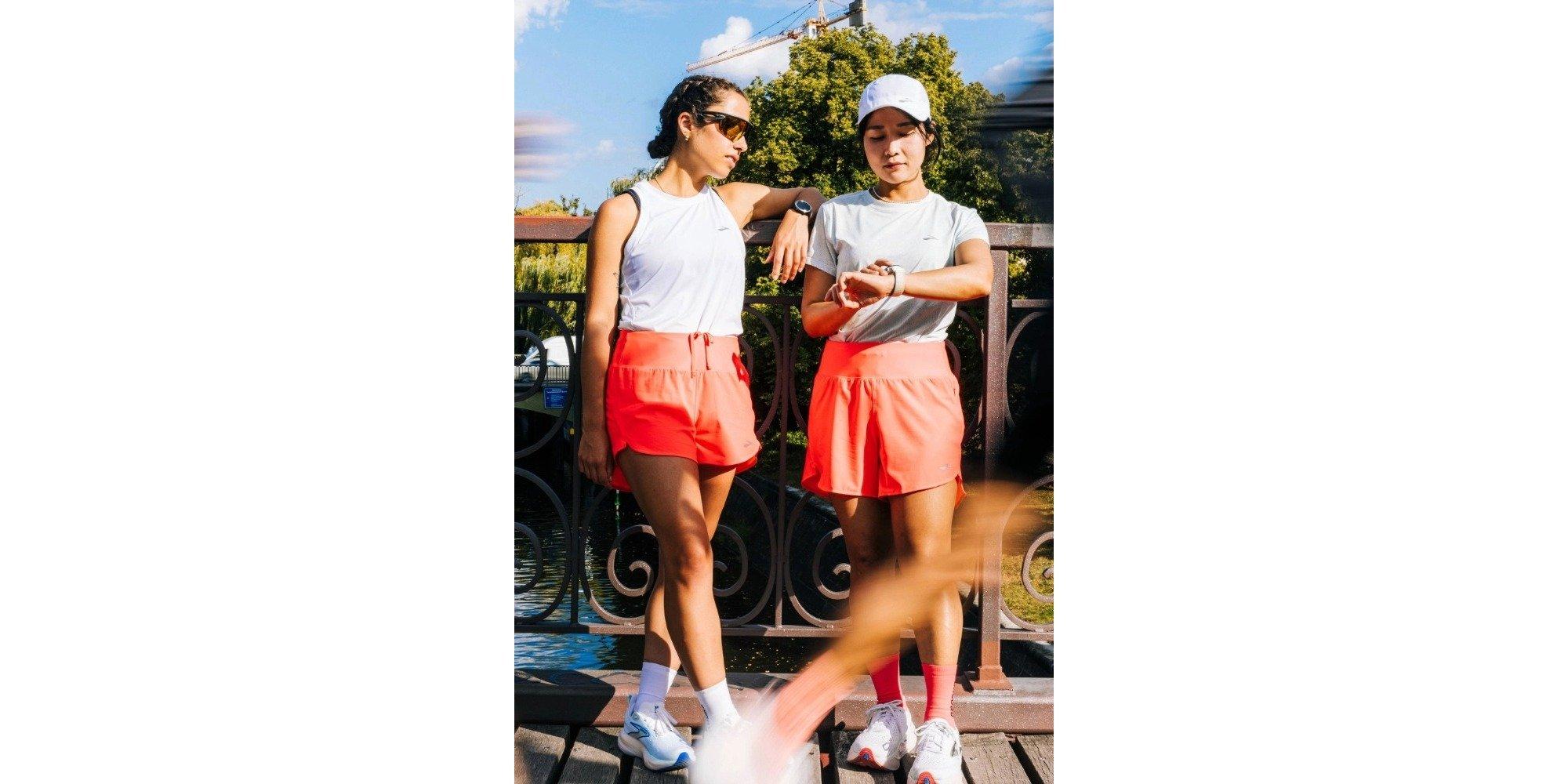 Two girls wearing running gear, standing against a bridge railing
