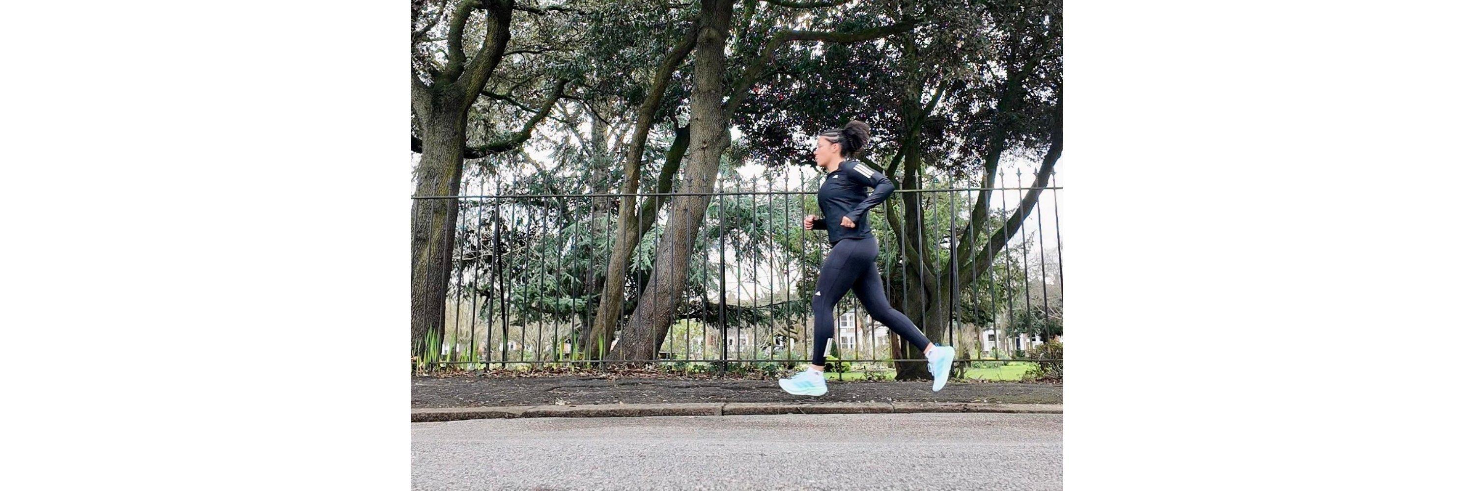 A picture of a women running on a road with a green park in the background