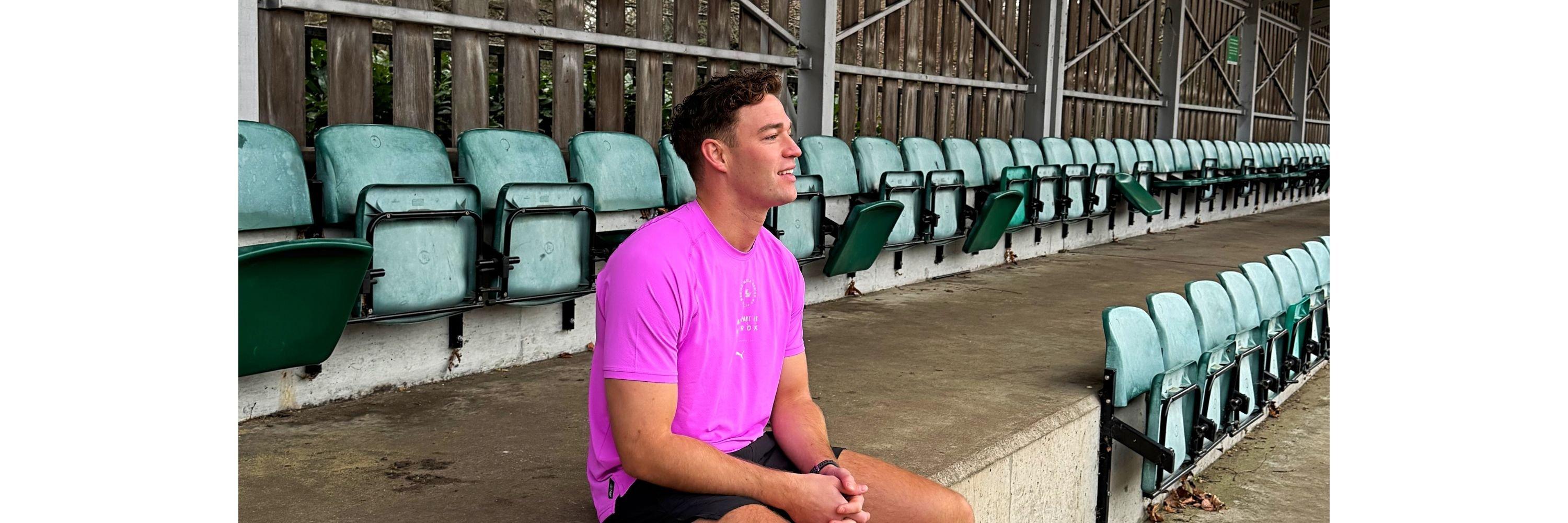 Ethan sat in the stands looking into distance wearing running gear