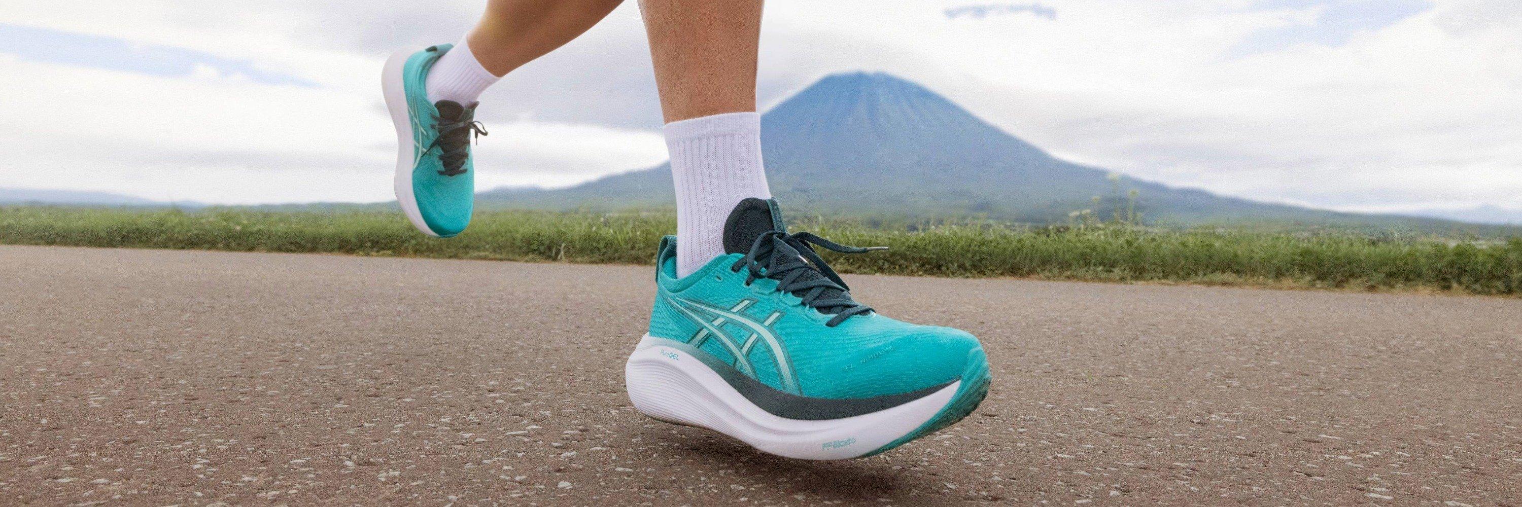 Image of someone running wearing blue running shoes with mountains and grass in the background
