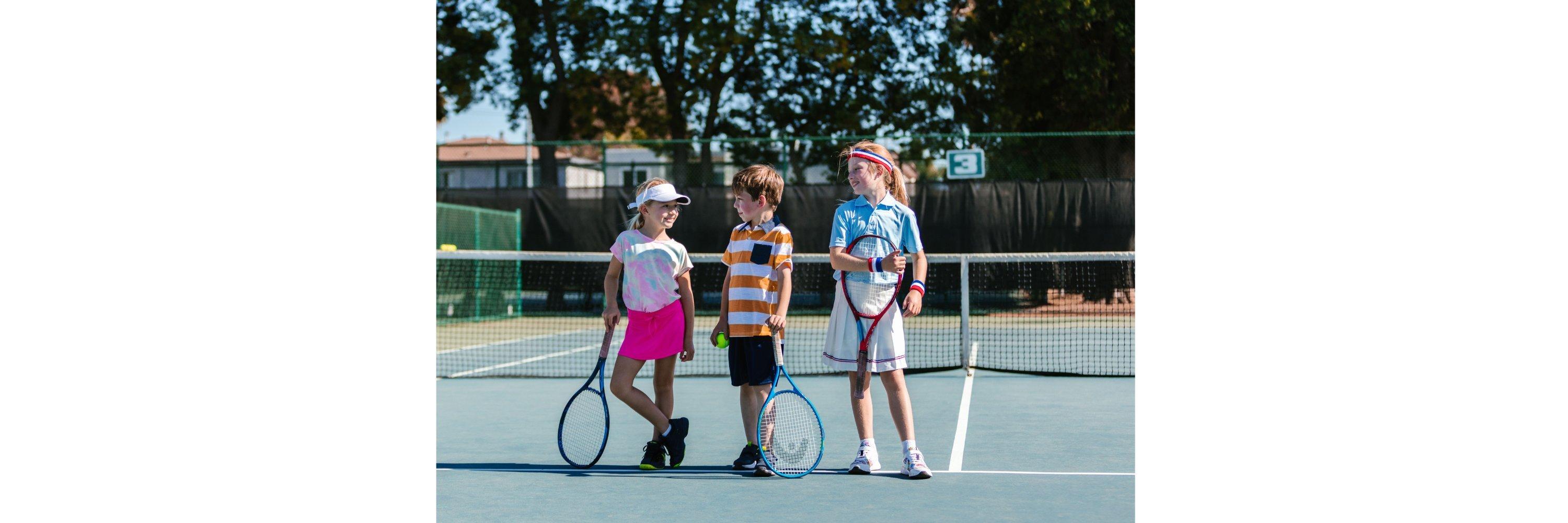 A picture of 3 kids on a tennis court holding tennis rackets