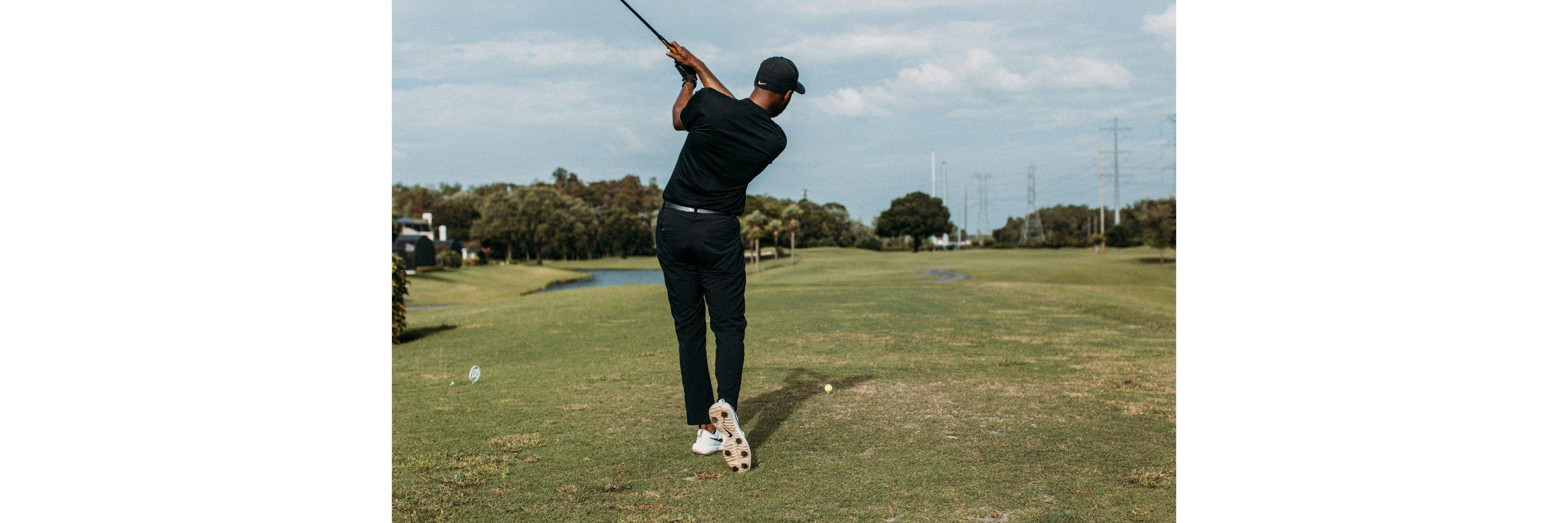 A man  on a golf course wearing golf clothes mid swing prior to hitting a golf ball