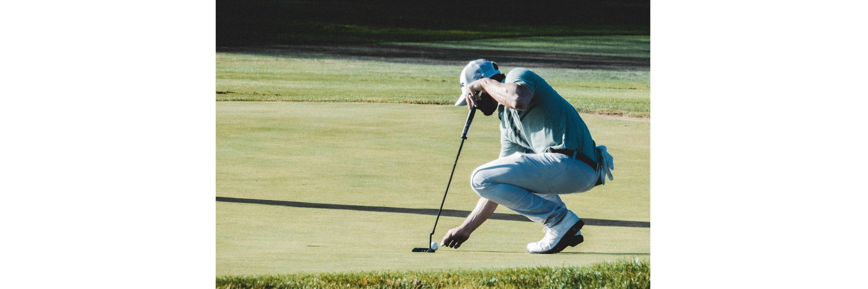 A man wearing golf clothes about to putt on a golf course