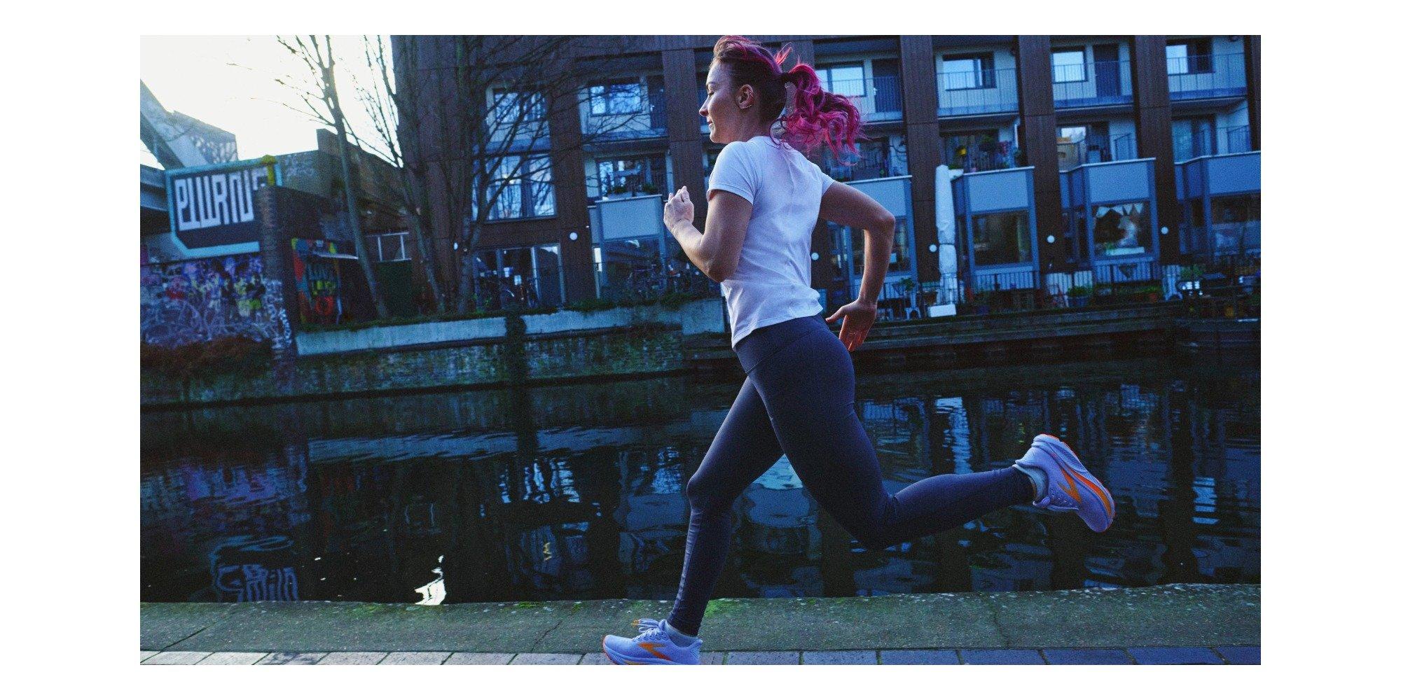 Woman running next to a river with apartments in the background