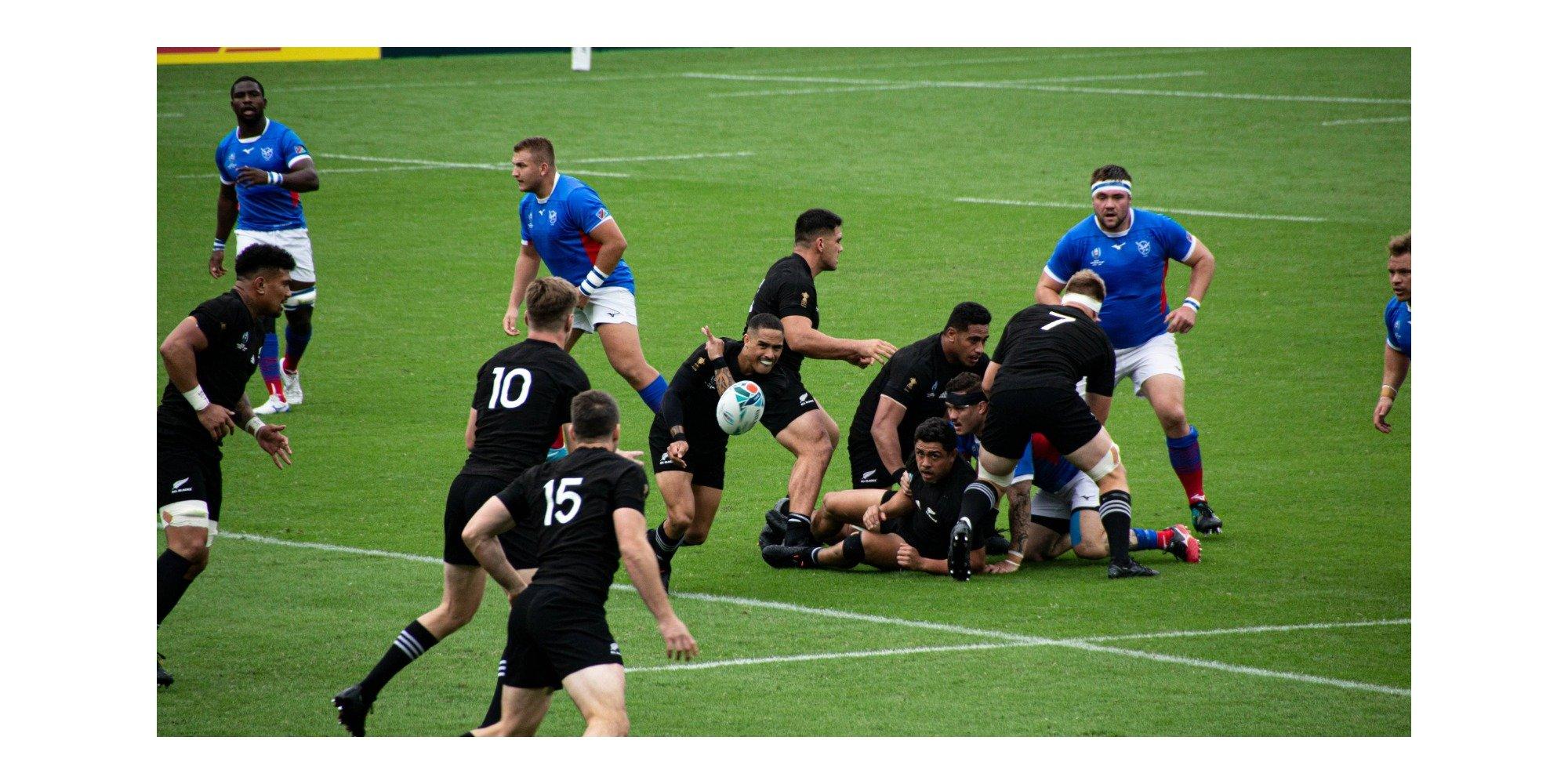 Two teams playing rugby, one team wearing black and the other wearing blue
