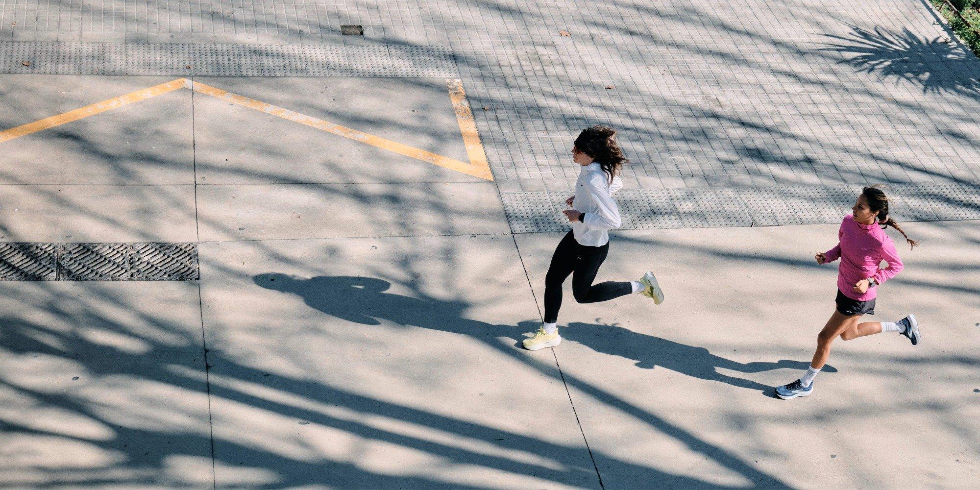 Two women running alongside a road, one running slightly behind the other
