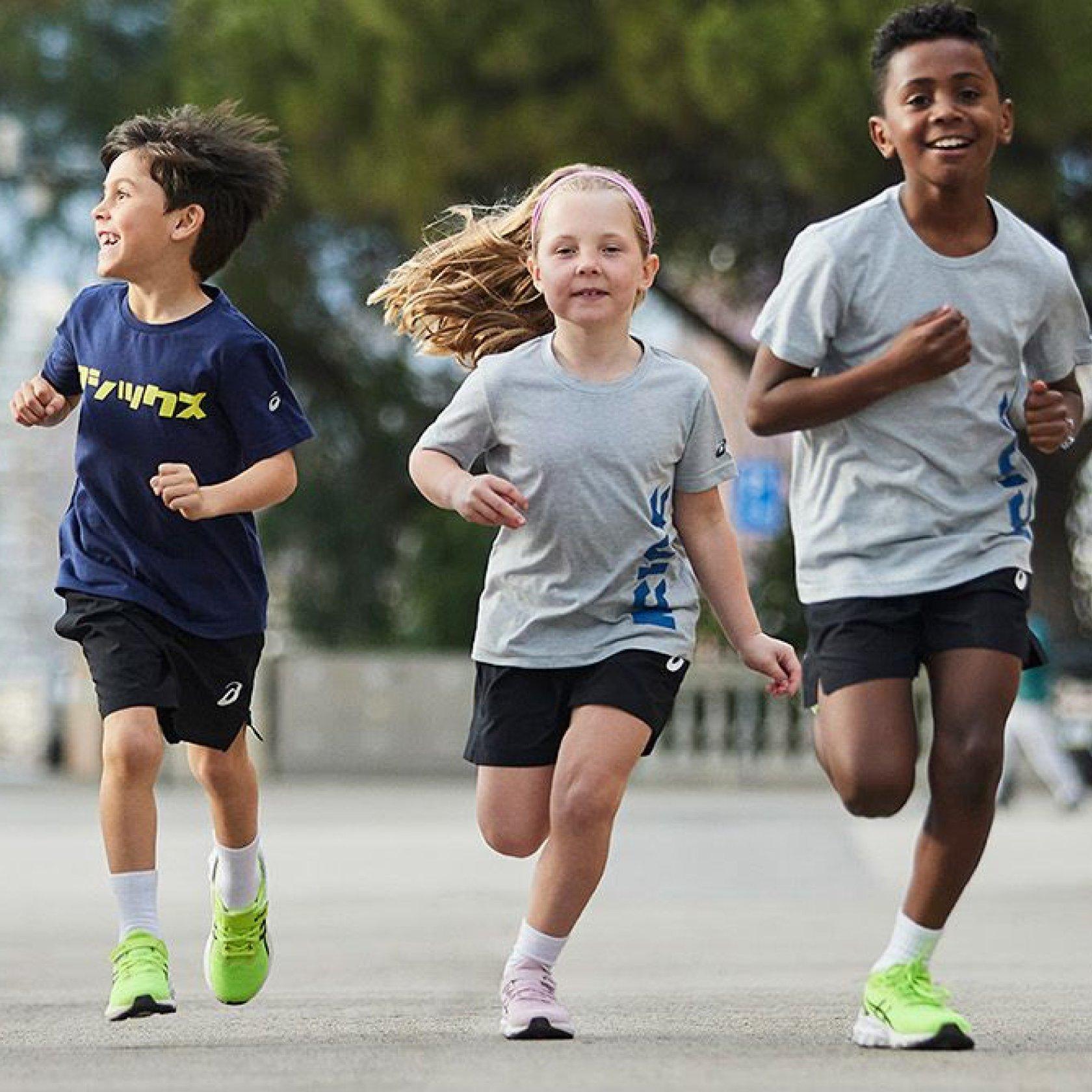 Bambini che corrono insieme all'aria aperta in abbigliamento e calzature Asics.