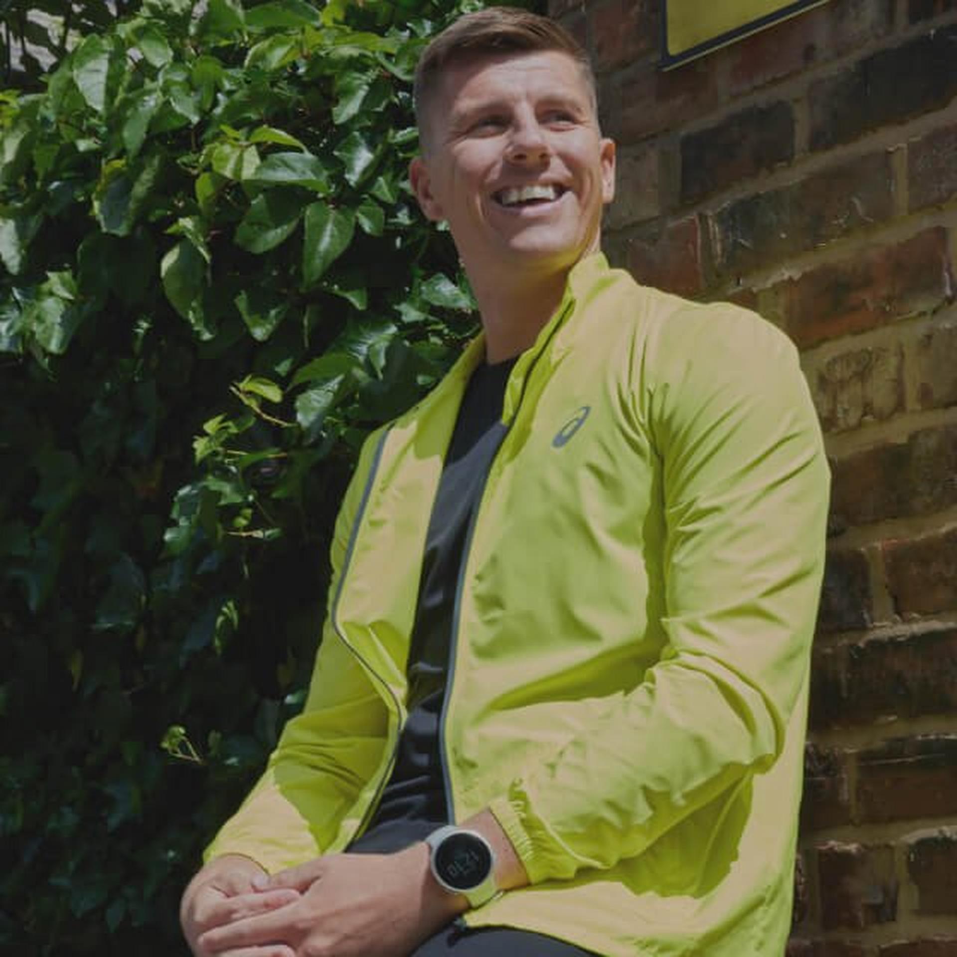 Man smiling while wearing a green Asics running jacket