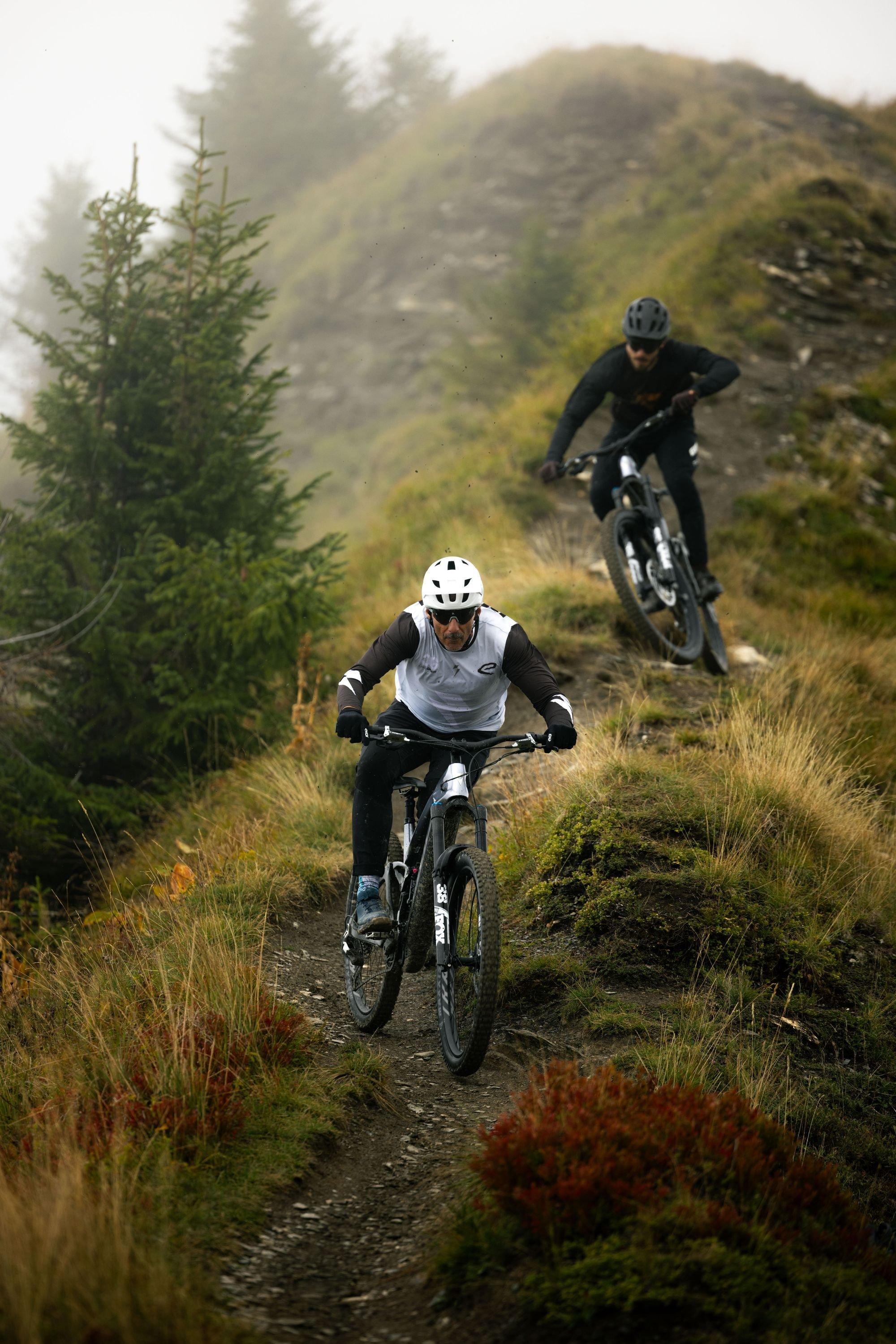 two mountain bikers riding down a steep hill on a foggy day
