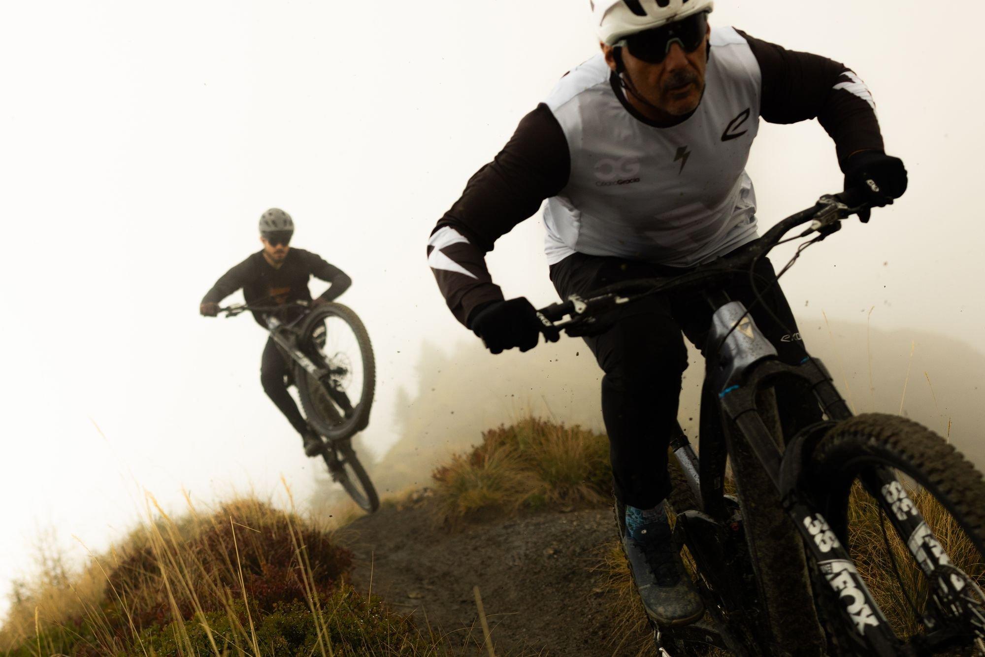 two men riding mountain bikes on a trail in the fog