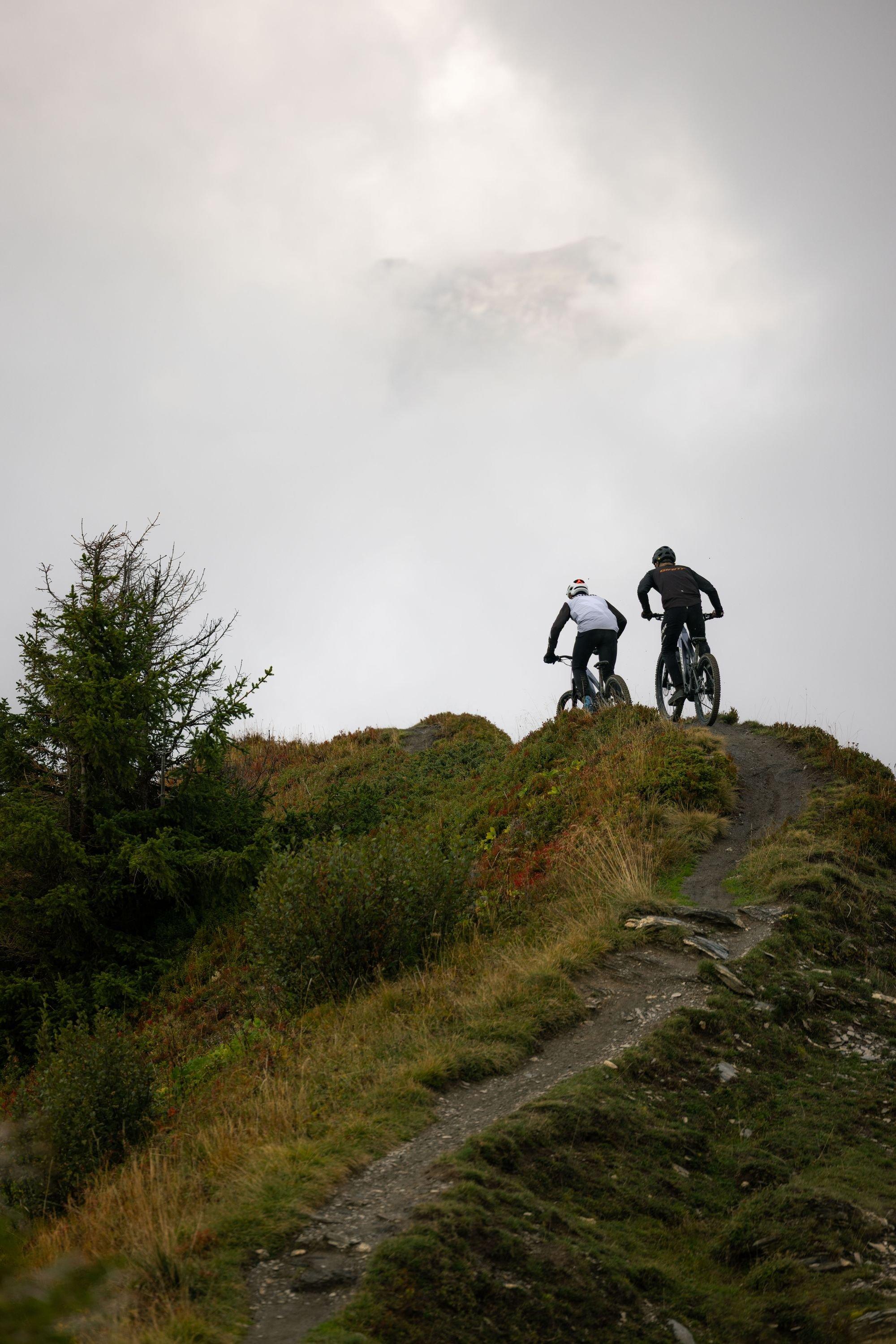 two people riding bikes on a steep hillside with a cloudy sky