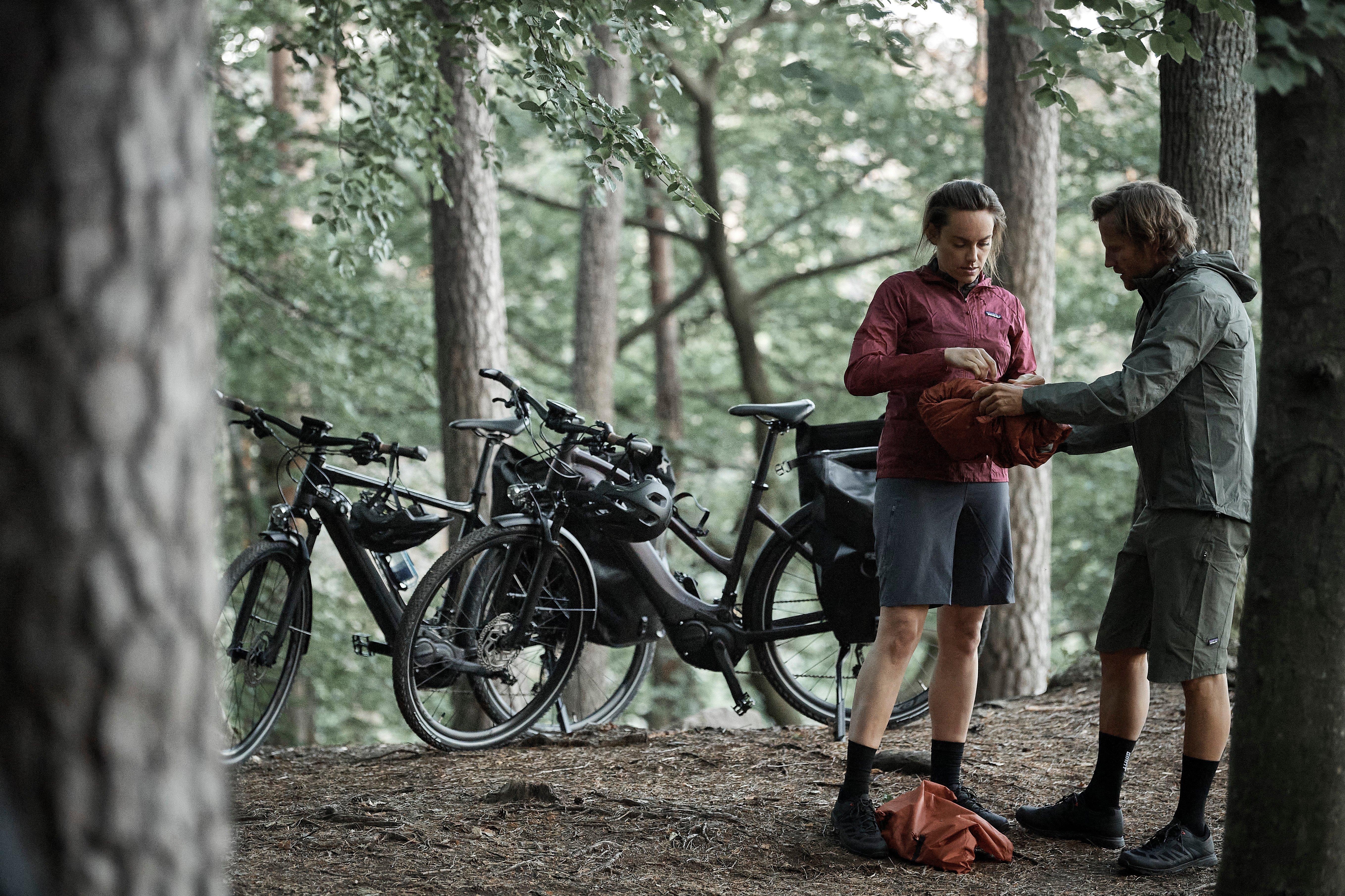 a couple of two people standing in the woods with their bikes